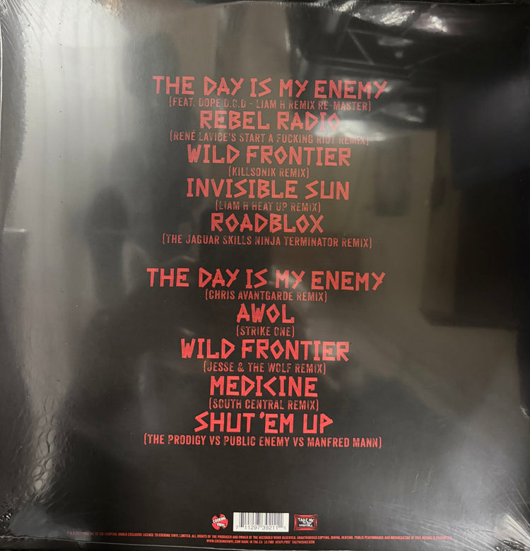 The back cover of a vinyl record sleeve, wrapped in protective plastic. The cover is black with a list of remix tracks in red text, including 'The Day Is My Enemy' and 'Rebel Radio'.