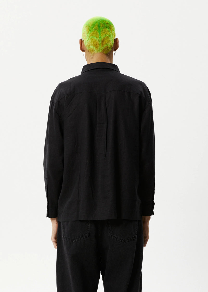 A male model wearing a long-sleeve black shirt with a traditional collar and button-up front, paired with black pants.