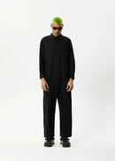 A male model wearing a long-sleeve black shirt with a traditional collar and button-up front, paired with black pants.