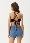 Woman wearing a black crop top with criss-cross straps and blue denim shorts on a white background