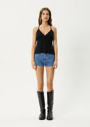 Woman wearing a black tank top, denim shorts, and black knee-high boots on a white background