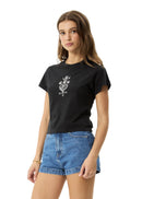 Woman wearing a black t-shirt with a white graphic design and blue denim shorts on a light gray background