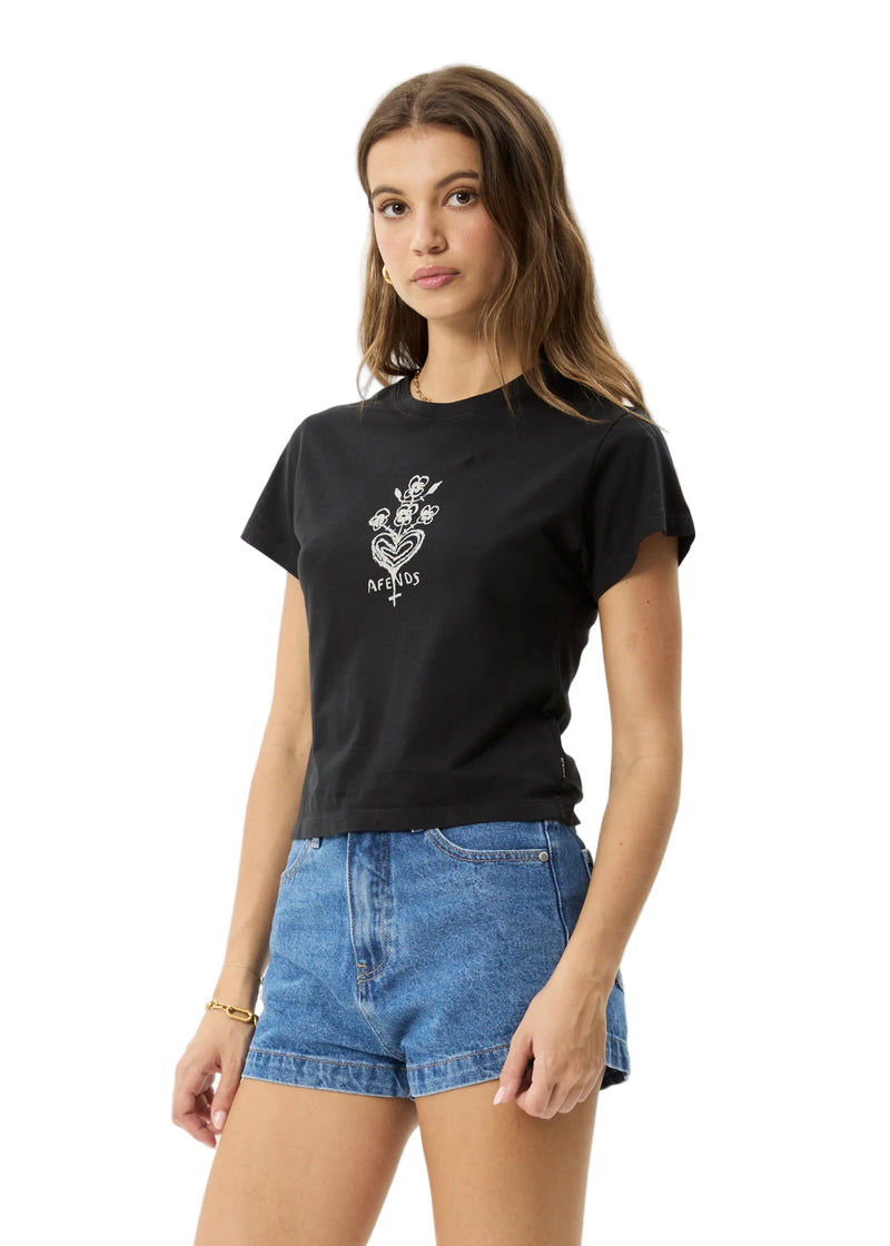 Woman wearing a black t-shirt with a white graphic design and blue denim shorts on a light gray background