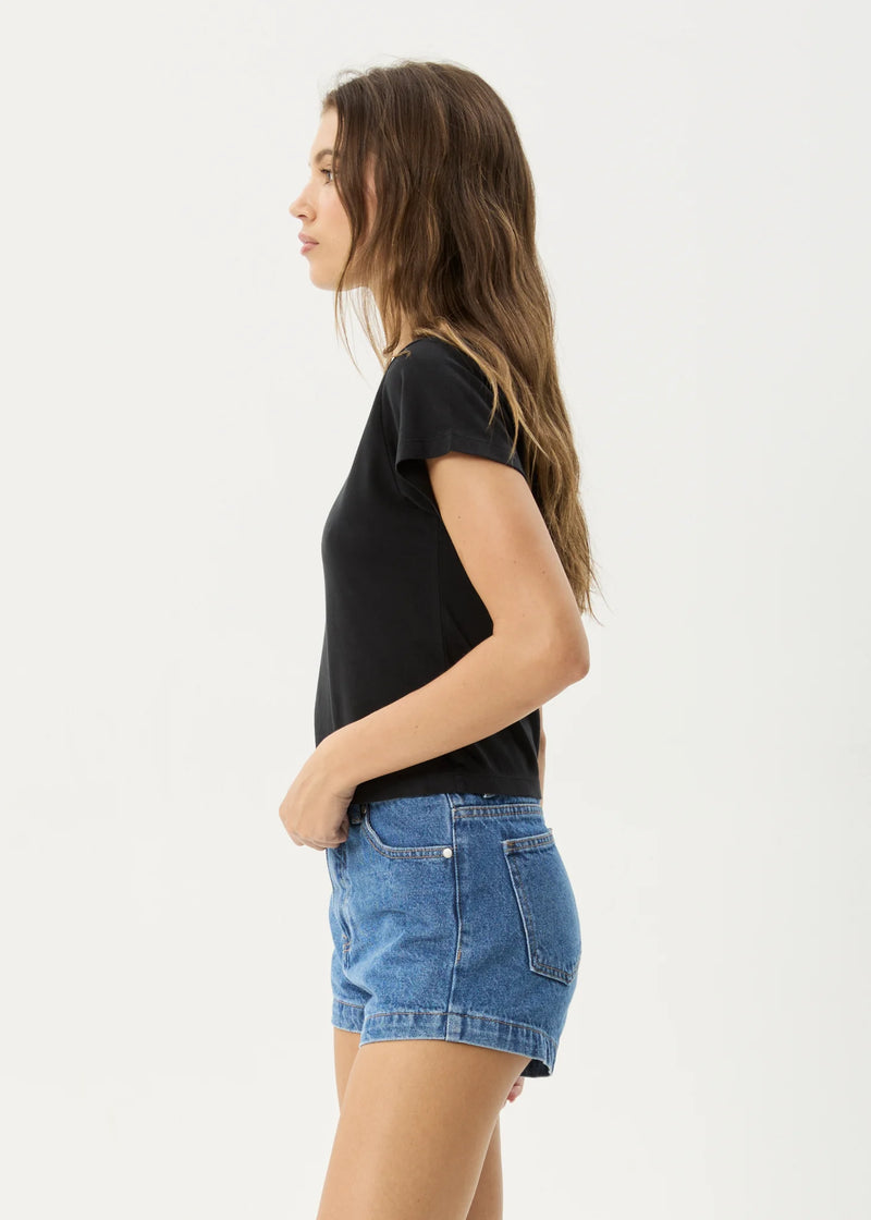 Woman wearing a black t-shirt and blue denim shorts on a white background