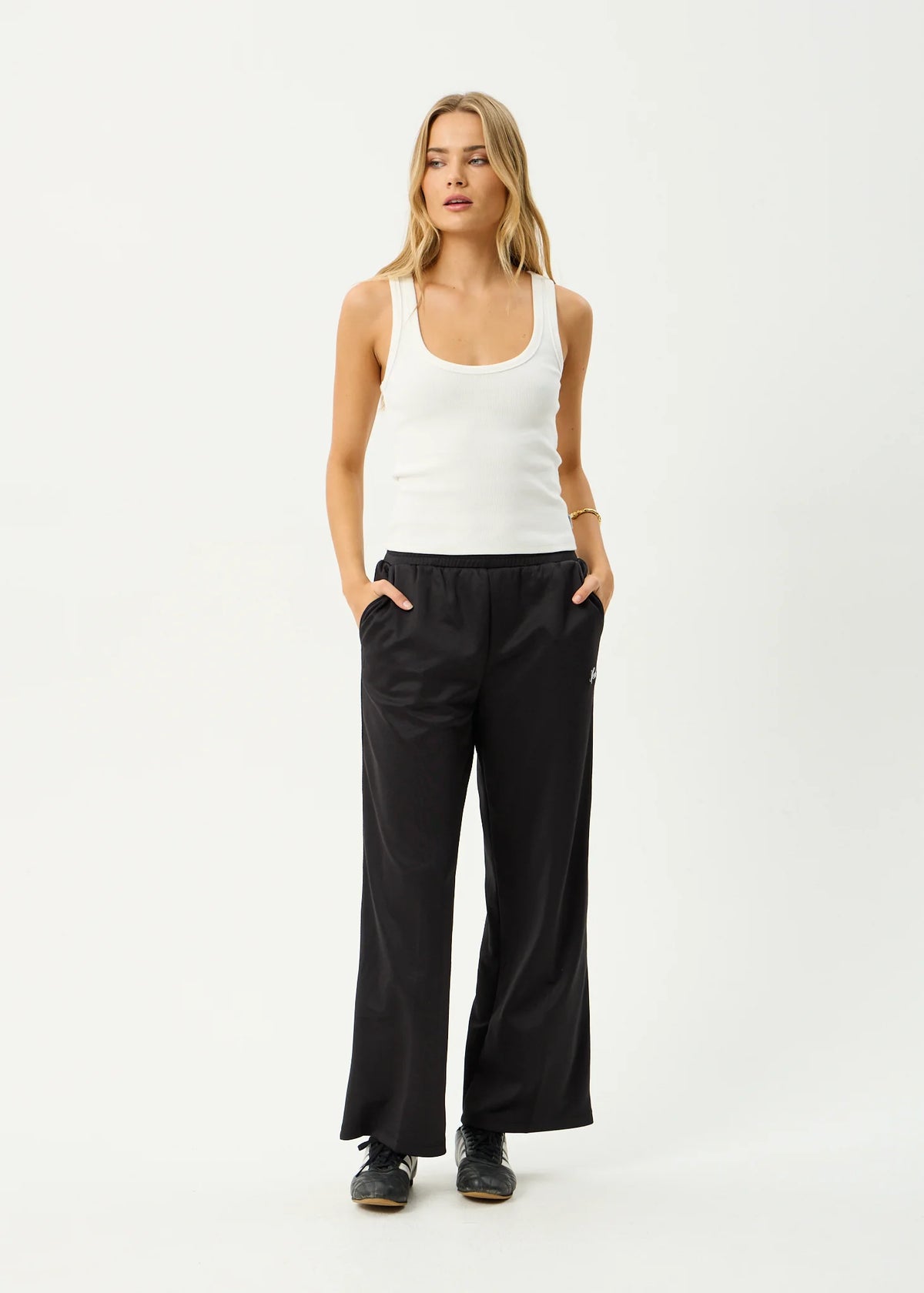 Woman wearing a white tank top and black pants on a white background