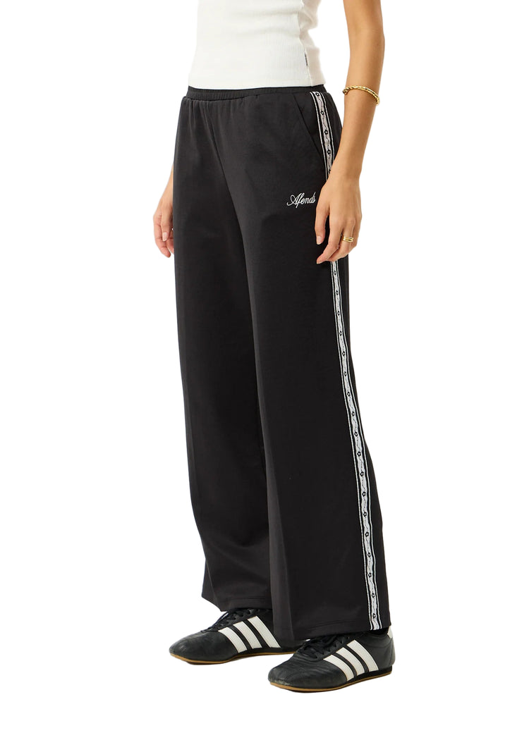 Person wearing black track pants with white stripes and Adidas shoes on a white background
