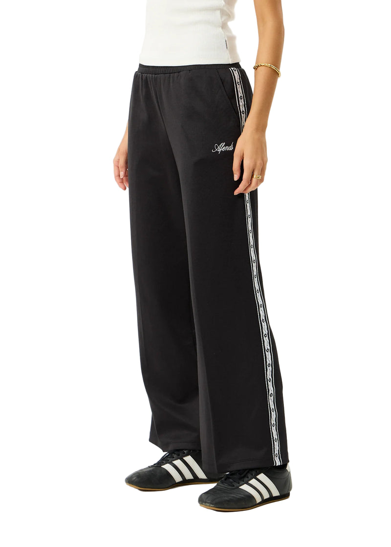 Person wearing black track pants with white stripes and Adidas shoes on a white background