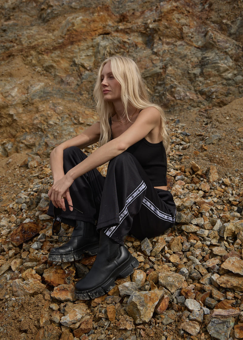 Person wearing black outfit with white stripes sitting on rocky ground