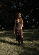 Woman in a brown dress standing in a grassy field with trees in the background