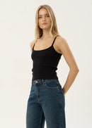 Afends Sara Rib Slinglet Black Woman wearing a black tank top and blue jeans on a white background