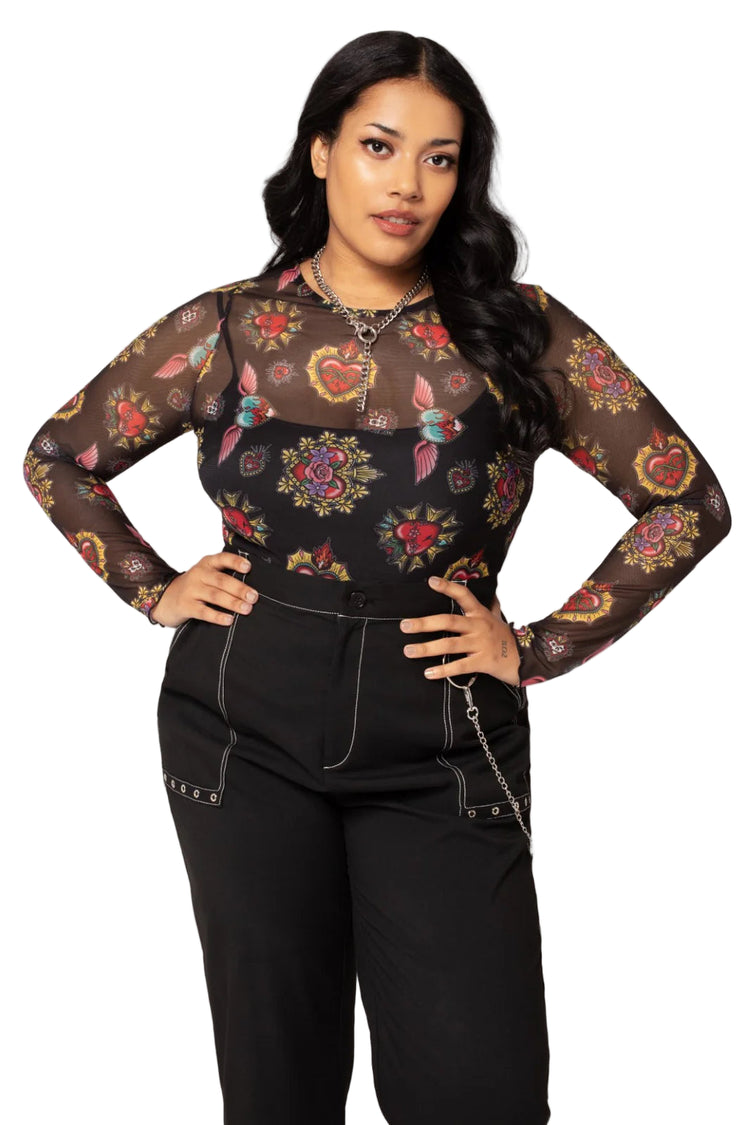 Woman wearing a black floral mesh top with black pants on a light pink background