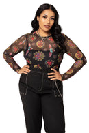 Woman wearing a black floral mesh top with black pants on a light pink background
