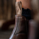 Close-up of a brown leather boot with a brand label on a blurred background