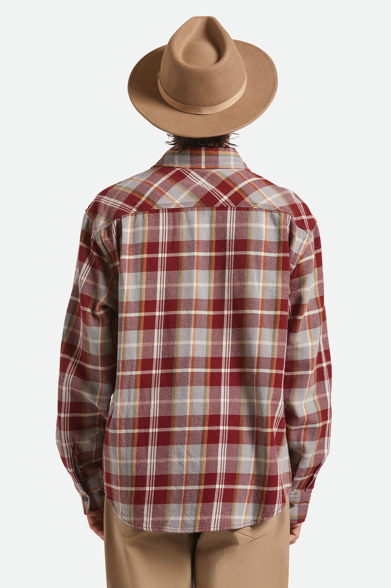 Person wearing a red and white plaid shirt with a brown hat on a light gray background