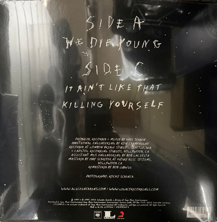 The back cover of a vinyl record for the album 'Side A: We Die Young Side C: It Ain't Like That Killing Yourself' by Pat Methacoli, shown inside its protective plastic shrink-wrap with reflections and dust specks visible.