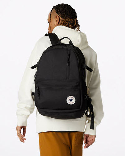 A person wearing a black Converse backpack with multi-functional pockets.
