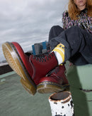 Person wearing Cherry red Dr Martens 1460 boots with yellow soles, sitting on a ledge with a cityscape in the background.