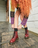 Person wearing cherry red Dr Martens 1460 boots and a colourful cardigan on a wooden floor.