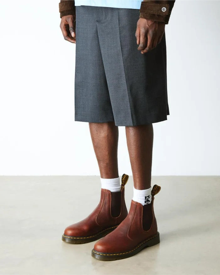 Person wearing brown Chelsea boots, gray shorts, and white socks on a plain background