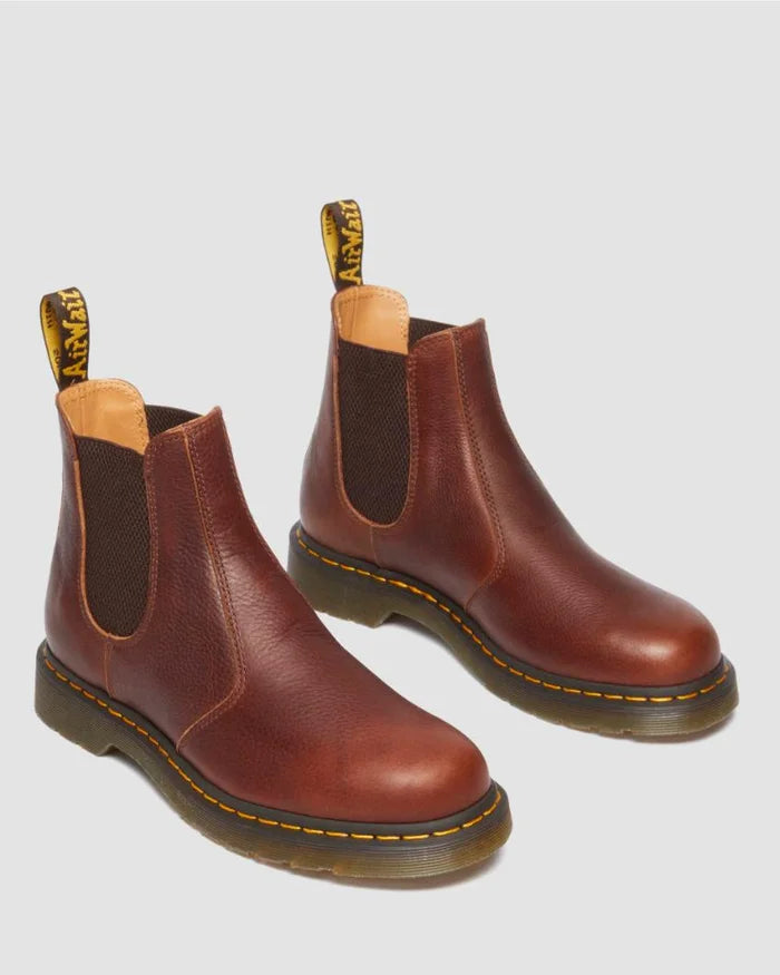 Pair of brown leather Chelsea boots with yellow stitching on a light gray background