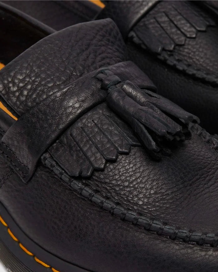 Close-up of Dr Marten Adrian black leather loafers with tassels and orange stitching.