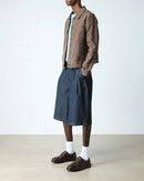 Person wearing a brown jacket, blue denim skirt, white socks, and Dr Marten Brookline brown shoes on a plain background