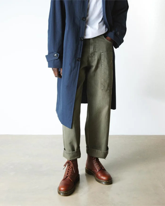 Person wearing a blue coat, white shirt, green pants, and brown boots on a plain background