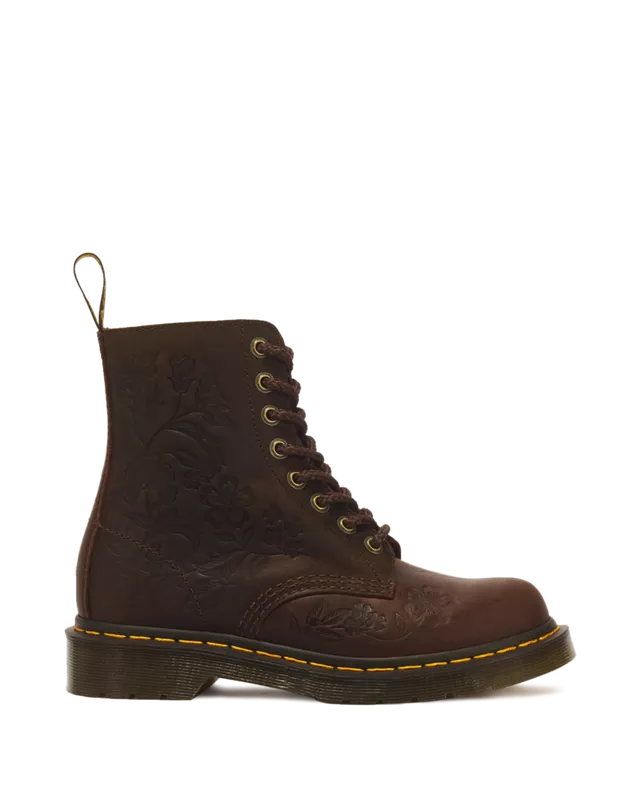 A single dark brown leather Dr. Martens 1-8/8 boot with floral embossing on the side, laced up with gold-toned metal eyelets, a yellow welt stitch, and a black sole, shown against a plain white background.