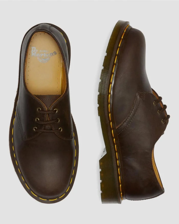 Brown leather shoes with yellow stitching on a light gray background
