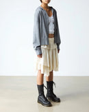 Person wearing a gray cardigan, white top, beige layered skirt, and black boots on a plain background