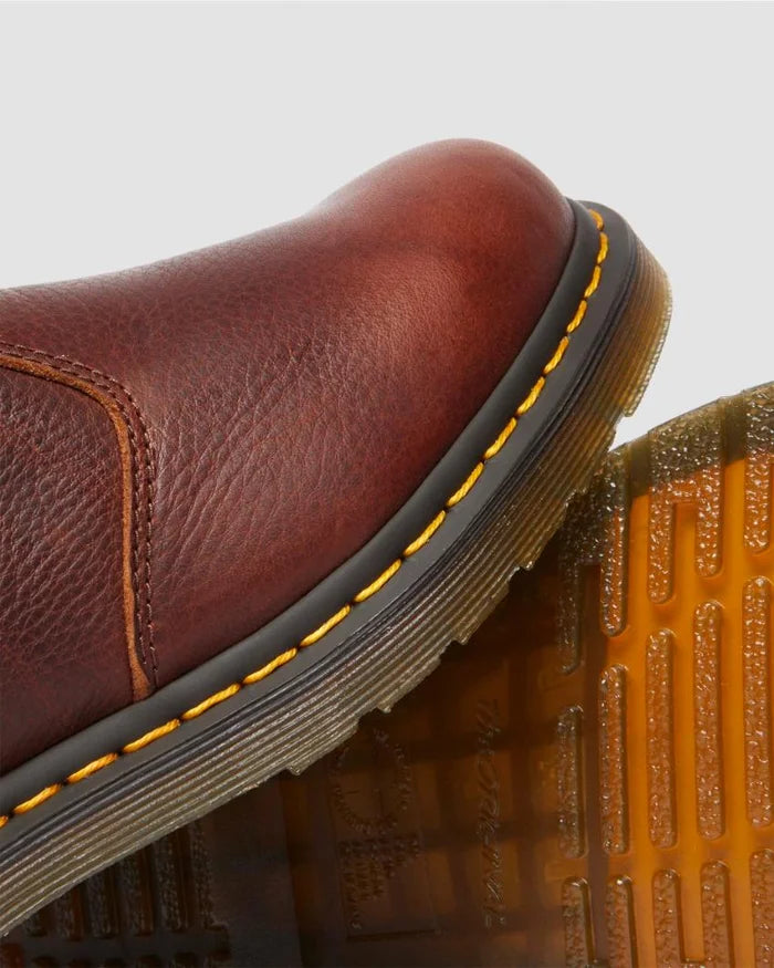 Close-up of a brown leather boot with yellow stitching on a light gray background