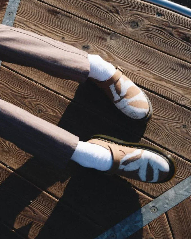 A pair of Dr Martens Archive Isham slip-on mules for women, featuring a hemp canvas vegan material in Savannah tan color with a floral print, antique gold hardware, and a Shore sole with yellow welt stitching.