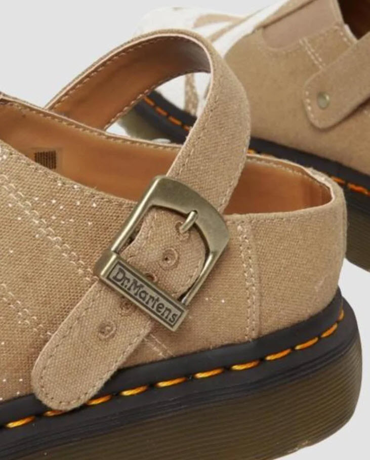 A pair of Dr Martens Archive Isham slip-on mules for women, featuring a hemp canvas vegan material in Savannah tan color with a floral print, antique gold hardware, and a Shore sole with yellow welt stitching.