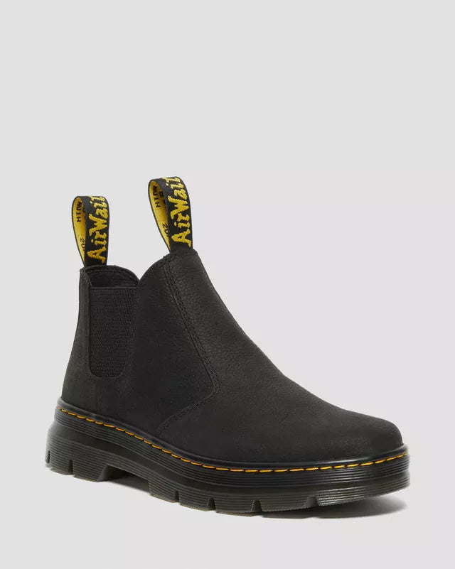 Black Chelsea boot with yellow stitching on a light gray background