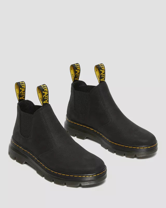Black Chelsea boots with yellow accents on a light gray background