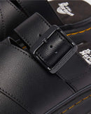 Close-up of a black leather boot with a buckle, featuring the Dr. Martens logo.