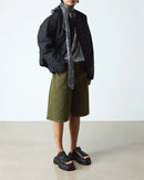 Person wearing a black jacket, gray shirt, green shorts, and black platform shoes on a white background