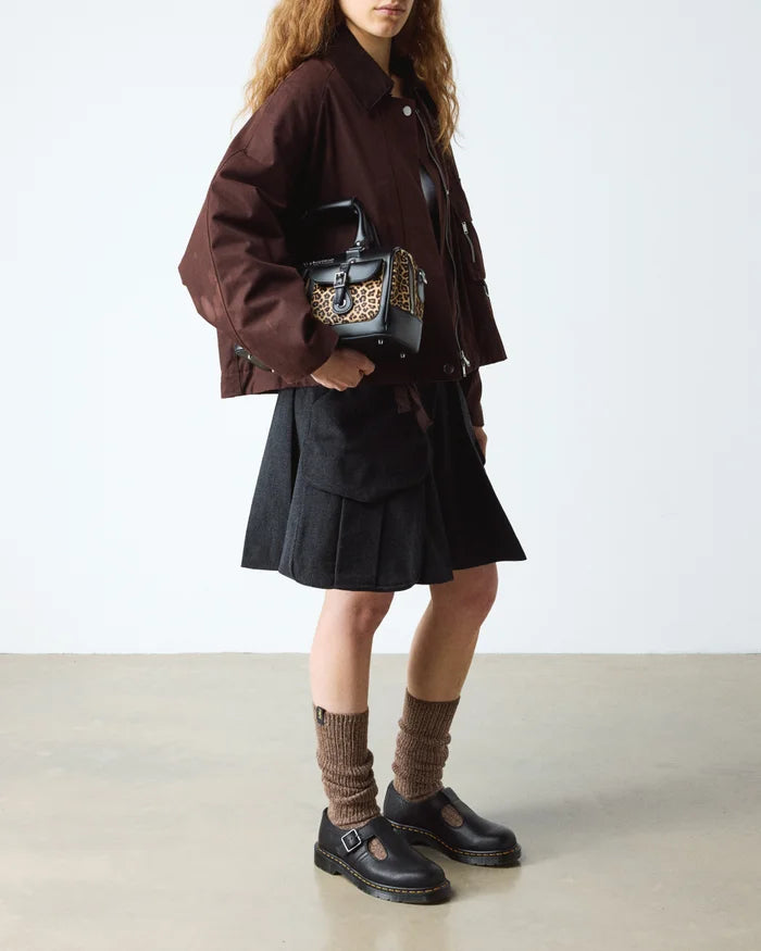 Person wearing a brown coat, black skirt, and black shoes with a patterned bag on a white background