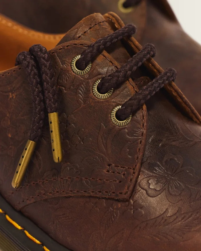 Close-up of a brown embossed leather shoe with dark brown braided laces and brass eyelets.