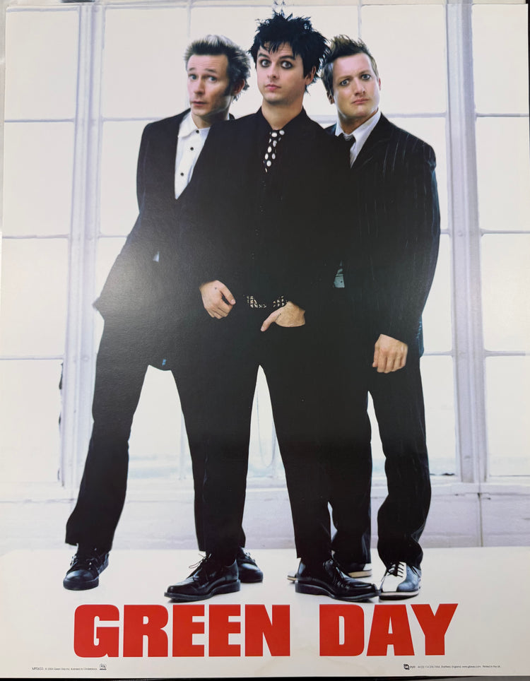 Green Day band poster featuring the three members in black suits standing in front of a bright white paneled wall, with the band name 'GREEN DAY' in large red letters at the bottom.