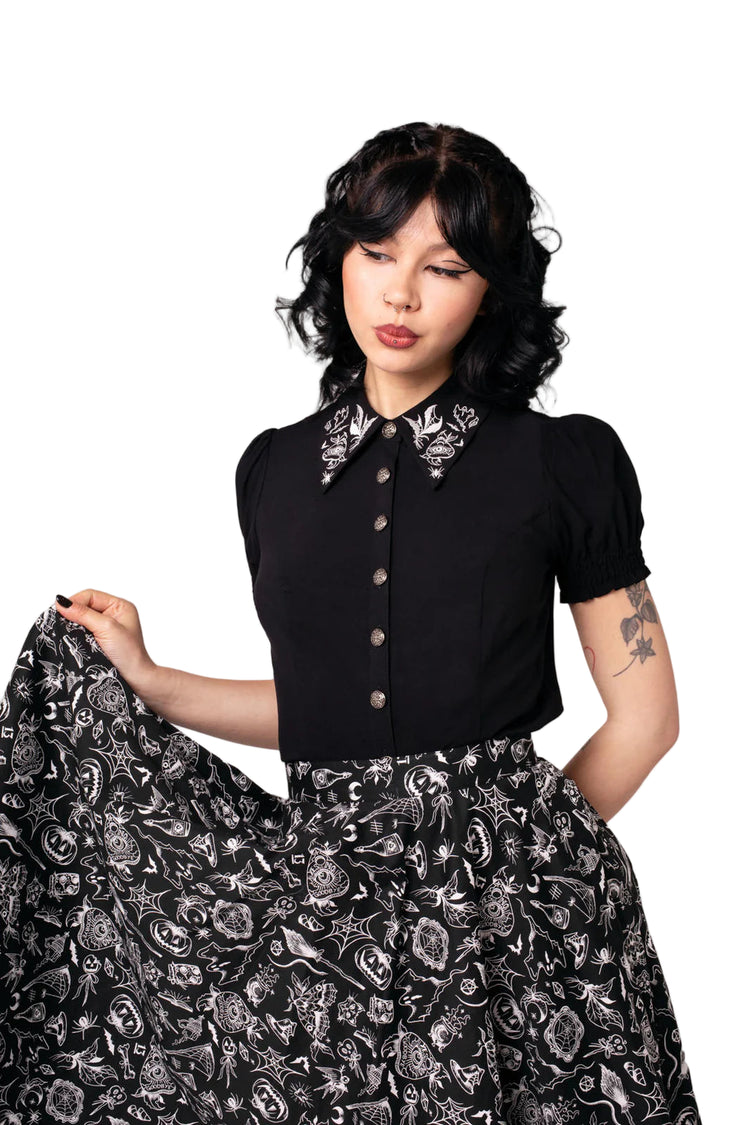 Woman wearing a black blouse with floral embroidery and a matching skirt against a light background