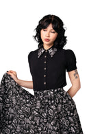 Woman wearing a black blouse with floral embroidery and a matching skirt against a light background