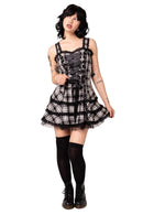 Person wearing a black and white plaid dress with suspenders on a white background