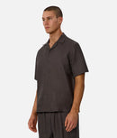 Man wearing a dark brown button-up shirt and pants on a white background
