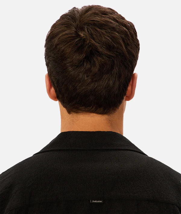 Back view of a person wearing a black shirt with a visible brand logo on a white background