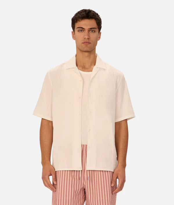 Man wearing a beige short-sleeve shirt and pink striped pants on a white background