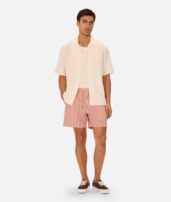Man wearing a cream shirt and red striped shorts on a white background