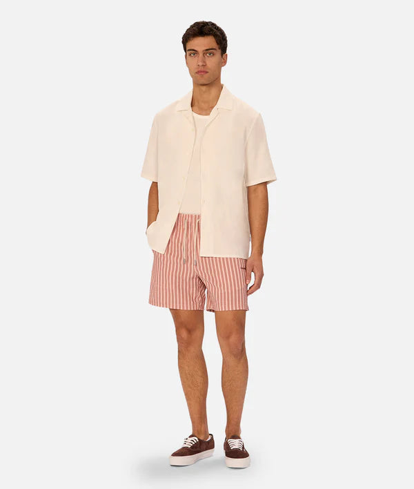 Man wearing a beige shirt and red striped shorts on a white background