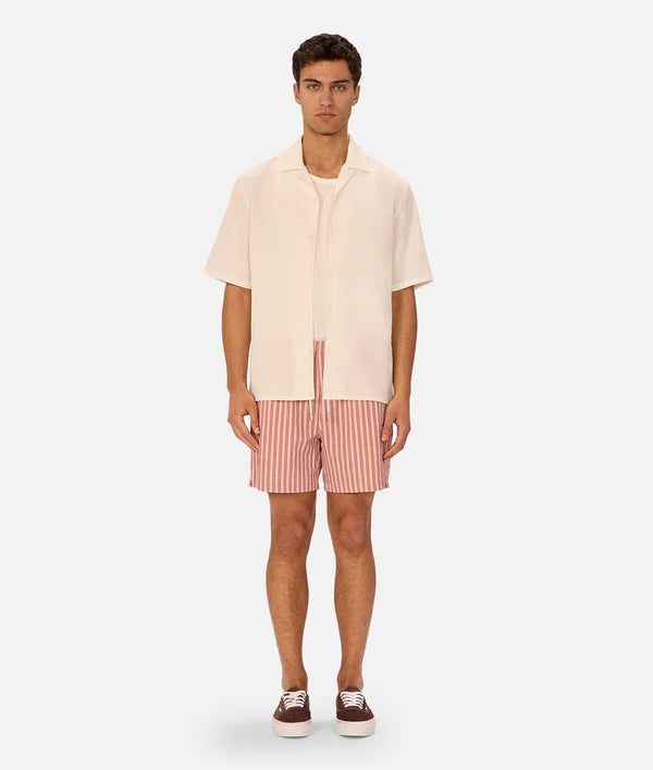 Man wearing a cream shirt and pink striped shorts on a white background