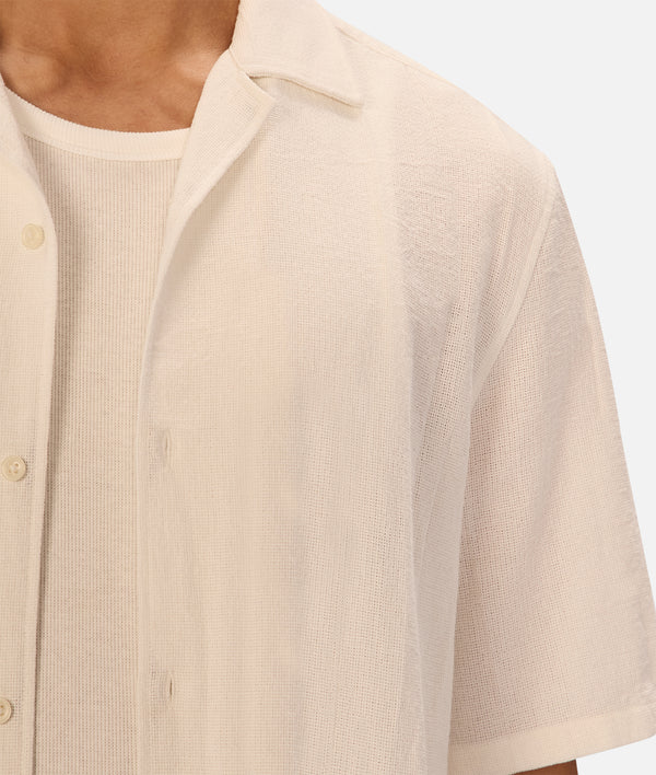 Beige short-sleeve shirt worn by a person on a white background